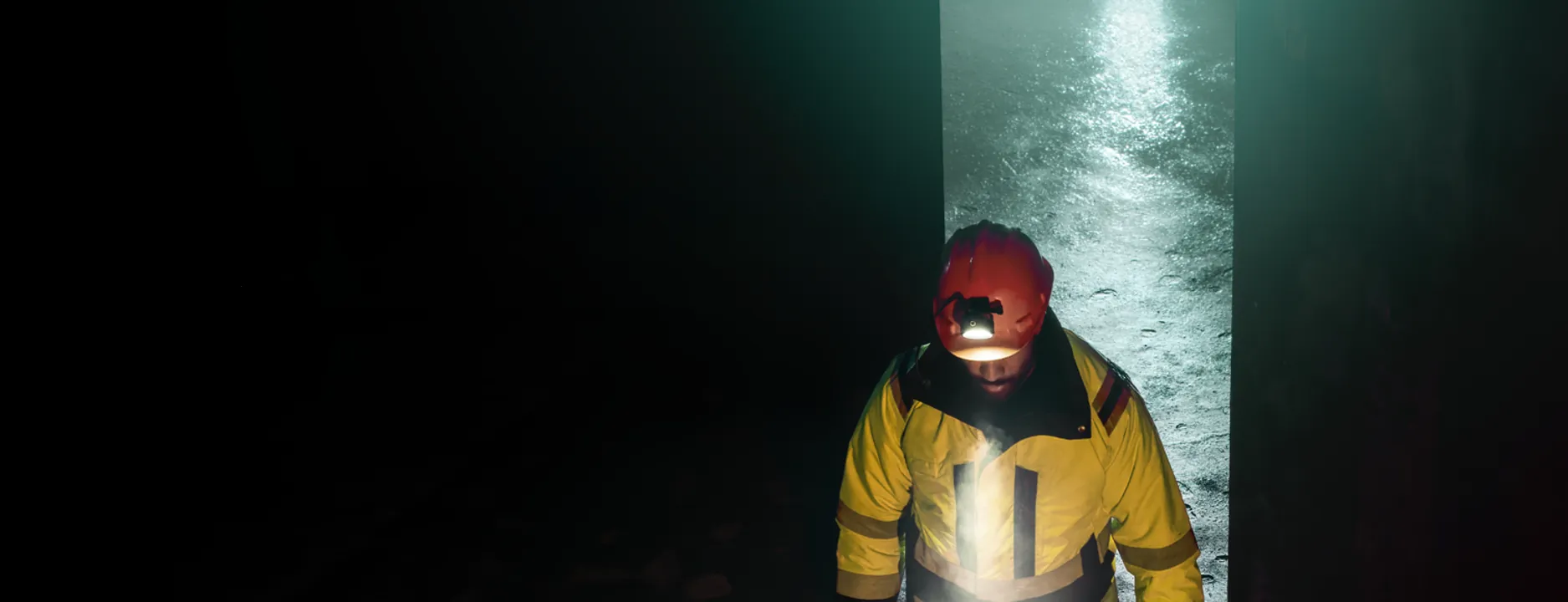 Strādnieks atstarojošā jakā un sarkanā aizsargķiverē ar lukturi tunelī