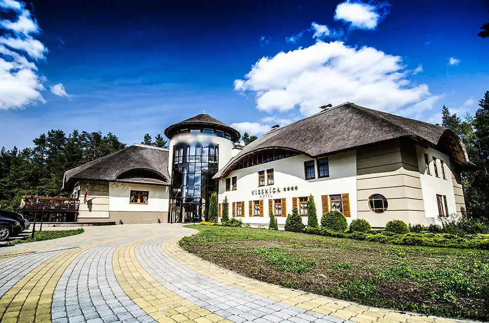 Molo Hotel ēka ar niedru jumtiem, stikla torni un priedēm zilās debesīs