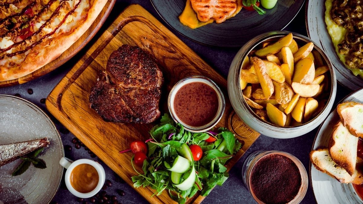 Grilled rib eye on a board with salad, potato wedges and pizza